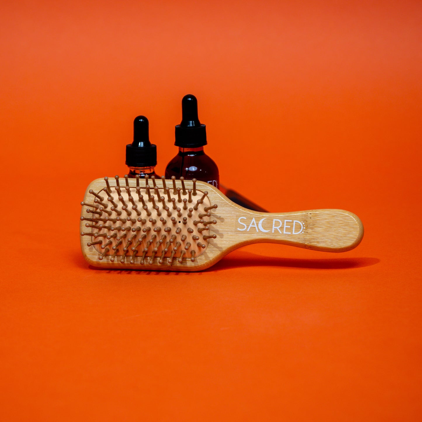 Wooden hairbrush and two bottles with droppers on an orange background