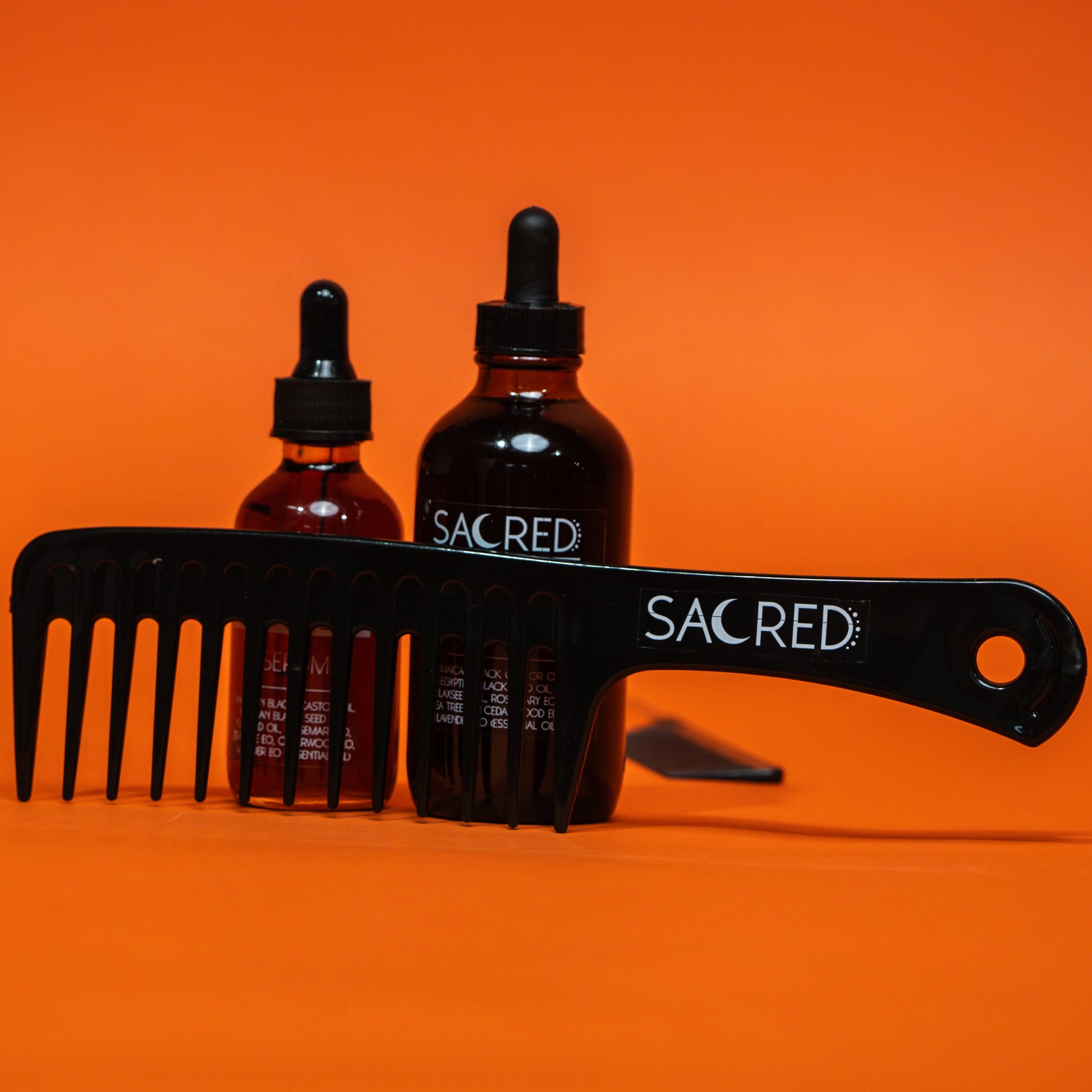 Two bottles of 'Sacred' hair care products with a comb and brush on an orange background